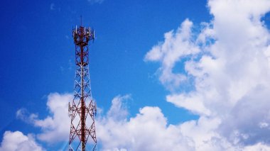 Yayılmış beyaz bulutlu, parlak mavi gökyüzüne karşı modern teknolojiyi gözler önüne seren yüksek bir iletişim yapısı..