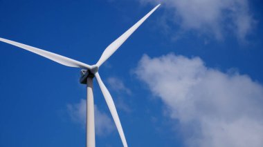 Rüzgâr türbininin parlak mavi gökyüzüne yakın çekim yaparak temiz enerji ve sürdürülebilirliği sembolize ediyor..