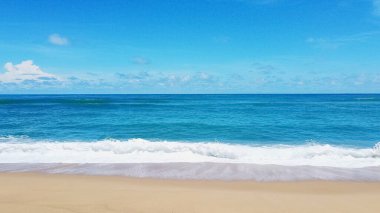 Altın kum, turkuaz okyanus dalgaları ve seyahat ve rahatlama temaları için mükemmel mavi gökyüzü içeren sakin bir sahil sahnesi..