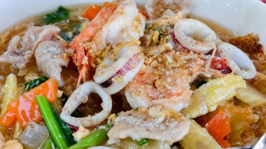 Lezzetli bir sos içinde karides, mürekkep balığı ve sebzelerin yer aldığı lezzetli bir Tayland deniz mahsulü eriştesinin yakın çekimi..