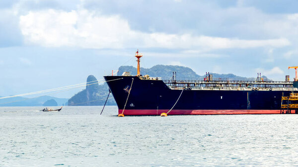 Большой грузовой корабль, стоящий на якоре в спокойных водах с горным фоном и облачным небом, демонстрирующий морской транспорт.