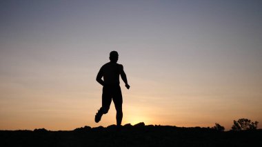 Gün batımında bir tepenin tepesinde sırt çantalı genç bir çocuğun silueti..