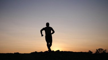 Gün batımında koşan genç bir adamın silueti..