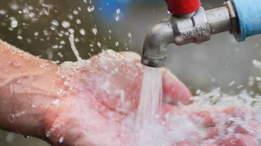 Banyodaki adam musluğu suyun elinde tutuyor.