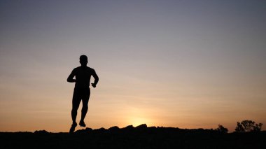 Sahilde koşan genç adamın silueti.