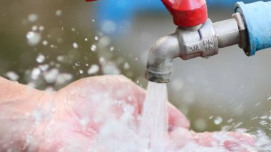 Eller açık bir musluğun altında, ferahlatıcı temiz suyun doğal bir ortamda yansımasını yakalıyor..