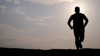 * * Gün batımı gökyüzüne karşı koşan bir insanın silueti, spor yapmayı, kararlılığı ve açık hava egzersizinin güzelliğini sembolize eder.