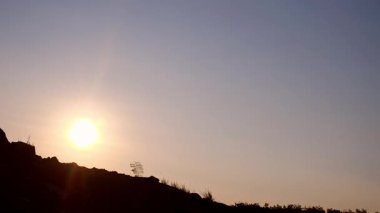 Sırt çantalı bir adamın silueti gün batımında dağda at sürüyor.