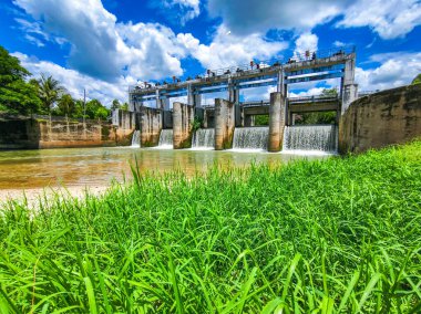 Şelaleleri çağlayan modern bir baraj, yemyeşil yemyeşil, ve güneşli bir günde mavi bir gökyüzü..