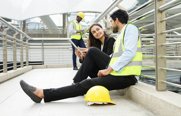 business engineer colleague chatting work by tablet online while sitting on walkway of building, engineer or architect working outdoor