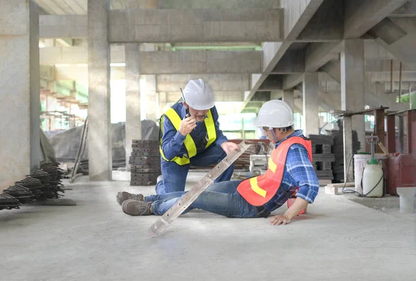 stock image construction young worker having an accident steel falls over legs while working on new house project, a senior man coworker using walkie-talkie communicate for help first aid support