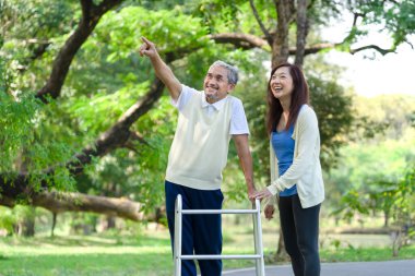 Baba ve kızı parkta yürümeyi seviyorlar, kıdemli adam Walker 'la yürüyor, babası işaret ediyor ve birlikte gülüyorlar. aile ilişkisi kavramı 