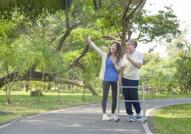 Baba ve kızı parkta yürümeyi seviyor, son sınıf öğrencisi Walker 'la yürüyor, kızı selfie çekiyor ve birlikte gülüyor. aile ilişkisi kavramı 