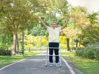 Yürüyüşçü kıdemli bir adam parkta yürürken el kaldırarak mutluluğu işaret ediyor. 