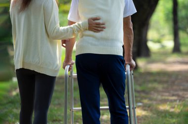 Yavru ya da bakıcı, engelli bir adamın el desteği bahçede Walker 'la yürürken düşmemesi, yaşlı yaşam tarzı, yaşlı toplum, yaşlı rehabilitasyon