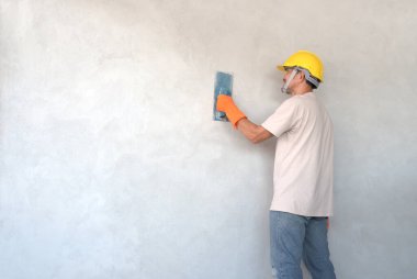 Keyfi yerinde olan bir adam beton duvarda duran sert şapka ve eldiven giyer. Endüstriyel iş konsepti, çimento işi, inşaat işi.
