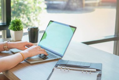 asian female hands typing laptop by glasses widow, coffee cup and note book on table 
