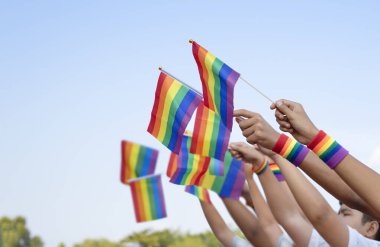 diversity of gays hands wear rainbow  wristbands holding lgbt flags up into the sky together, represents to unity of gay community and freedom.concept lgbtq happy pride month in june