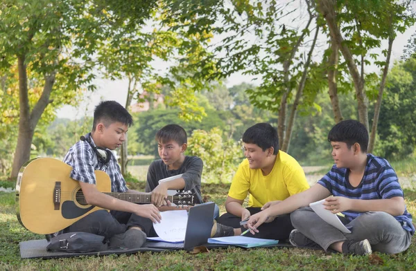 teen boy holding guitar,helping his three school junior boys to play and compose music,happy asian teenagers playing music together,concept for teenagers adult helping junior to do school arts project