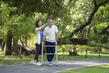 disabled senior man walking with walker, happy family, father and daughter enjoy talking and exercising in the public park, concept of daughter helps disabled father to exercise, elderly health care, wellness, wellbeing