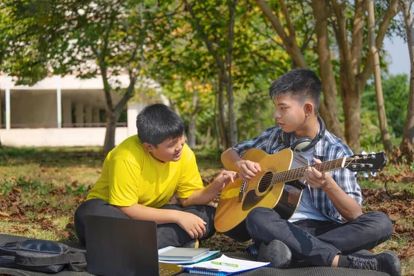 teens male playing music and compose music together,asian teenager boys sitting on matt at school backyard,doing school arts work project