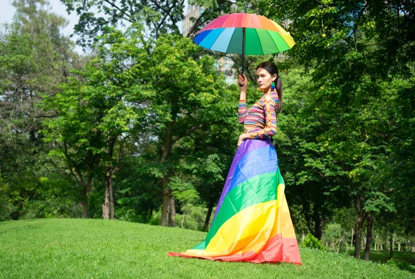 concept lgbtq community equality movement, proud to be gay, lgbtq happy pride month, portrait young transgender woman in colorful rainbow dress raising umbrella in the park