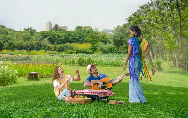 group of friends having a picnic in the city park, young asian gender diverse enjoy playing music and dance during picnic on their weekend