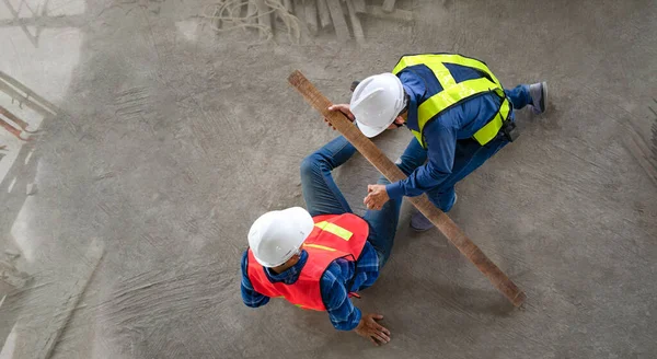 accident in site work,a piece of wood fell from height hit on a worker\'s legs while working at a new building, a colleague rescued him from  accident.concept risk management, safety at work