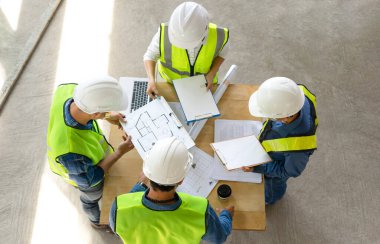 İnşaat halindeki binada dizüstü bilgisayar, planlar ve belgeler kullanarak mühendisler toplantısının en üst görüntüsü, iş arkadaşlarıyla proje yöneticisi istişare toplantısı