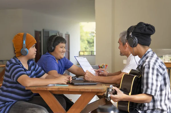 group of teenage students learning music with mature artist teacher,asian senior explained sheet music to teens pupils,concept adult help teenagers to do school music project