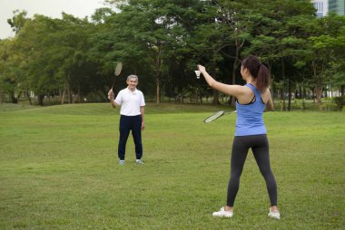 Genç bir kadın parkta yaşlı bir adamla badminton oynuyor (seçici odaklanma), kız babasıyla açık hava aktiviteleri geçiriyor, konsept insan yaşam tarzı, spor ve eğlence, aile ve aile ilişkisi