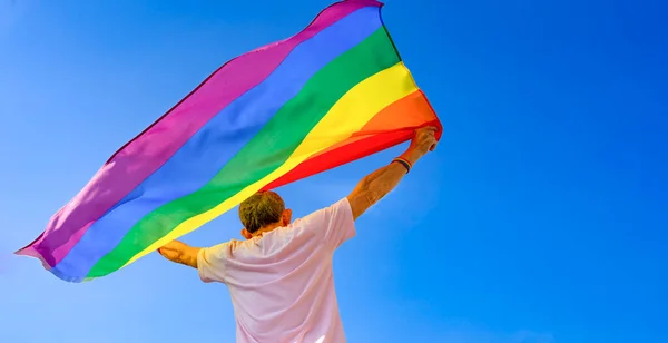 mature man holding colorful lgbt rainbow flag raising up into the air the meaning of freedom background blue sky, concept for support community equality movement lgbtq+, lgbtq happy pride month