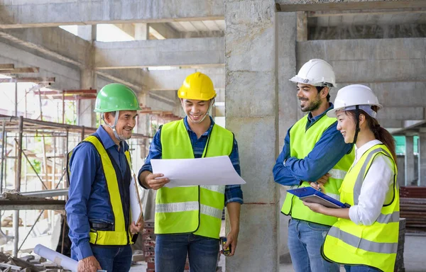 Mühendis proje yöneticisi yeni bina inşaatının yapısal standartlarını inceliyor. İnşaat alanının altındaki binanın dışında çalışan güvenlik üniformalı mühendisler.