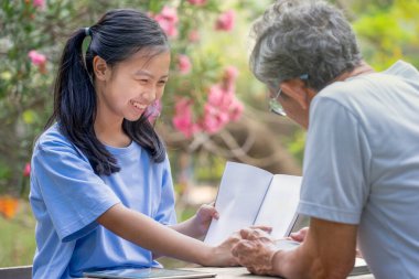 Asyalı genç kız büyükbabasıyla parkta kitap okurken eğleniyor, torunu büyükbabasıyla gülüyor ve konuşuyor, aile kavramı, aile sevgisi, ergen yetiştirme