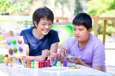 Orta yaş resim öğretmeni, okul sanat kulübünde genç bir çocuğa resim öğretmekten hoşlanır. Asyalı bayan öğretmen, resim dersinde genç öğrencilere yardım eder.