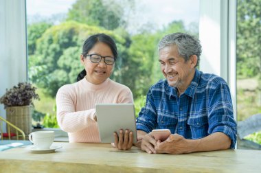 Asyalı üst düzey çiftler internette birlikte sörf yapmayı severler. Yaşlı yetişkinler evde kahve molası verirken internetten tablet internete bakıp birlikte oturup gülerler.