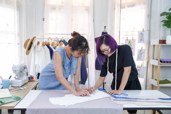 young confident female designer in purple color hair discussing about clothes pattern with tailor at fashion studio, concept of business,industry,design,tailoring