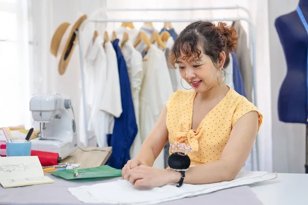 beautiful young asian female working in fashion studio, a smiling experienced tailor is tailoring clothes at her own shop,concept of fashion design,sewing,craft,tailoring,business,industry