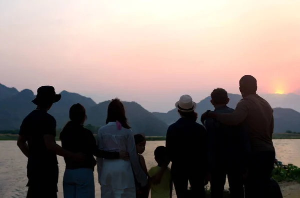silhouette back view group of family standing by the river,looking forward to the beautiful sunset on mountain, close friend two family travel together,people relax in nature