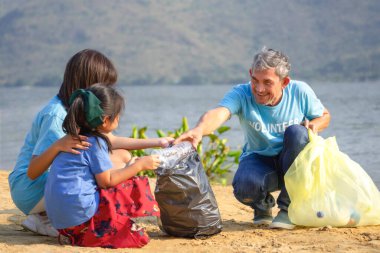 Dedem plastik şişe tutuyor. Çocuklara kum sahilindeki çöpleri ayırmayı öğretiyor. Plastik şişeyi tekrar kullanmak için topluyor ve ayırıyor. 