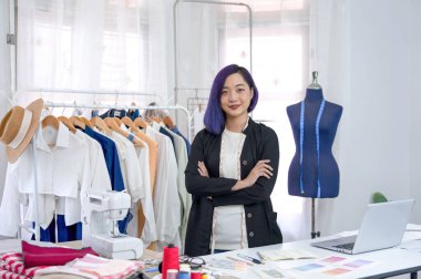 Mavi saçlı, kollarını kavuşturmuş genç, havalı Asyalı kadın tasarımcı. Giysi moda stüdyosunda çalışırken gülümse. Kıyafet tasarımı konsepti, terzilik sektörü.