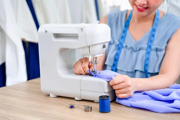 happy young asian female sitting with sewing machine,working, smiling experienced tailor is sewing clothes at factory,concept of sewing,worker,working,craft,tailoring,dressmaking,business,industry