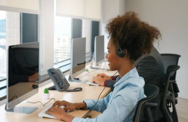 Afro-Amerikan kadın kulaklıklar bir çağrı merkezinde çalışıyor, iş kadını operatör telefona internetten cevap veriyor.
