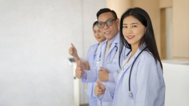 Üniformalı asistan takım çalışması yapan, gülümseyen, baş parmağını kaldıran ve metin için fotokopi alanı olan bir hastanenin önünde duran doktorlar.