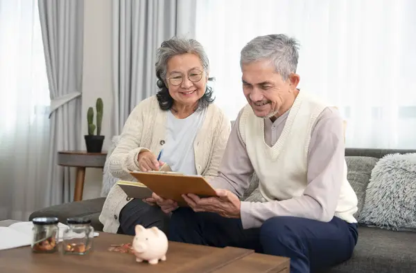 asian senior couple is looking for savings plan together,old man holding money savings chart,his wife holding note book,they are smiling happily,concept of money management in elderly people,savings