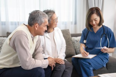 Asyalı üst düzey çift, ev ziyaretçisi bir hemşireyle konuşuyor, civayı ölçen ve not alan genç bayan hemşire, yaşlılar yaşam tarzı, ev bakımı, ev sağlığı hemşireliği kavramı 