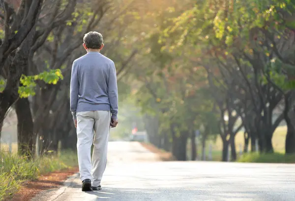 senior man walking along the street in the morning sunshine, in autumn park