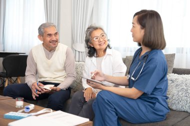 Asyalı yaşlı çift, evde misafir hemşireyle, genç bayan hemşireyle konuşuyor, tablet, yaşlılar yaşam tarzı, ev bakımı, evde sağlık hizmetleri gibi konuları kullanarak evde kişisel sağlık hizmetleri hakkında tavsiyelerde bulunuyor. 