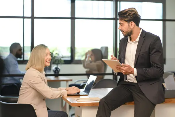 young multi ethnic business people discuss work in the company office,white businessman sitting on table casual talking work with asian businesswoman colleague by using tablet