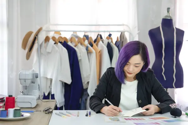 young cool female designer with purple color hair concentrate to create sketching and color comparison of clothing design on table,a professional dressmaker working in modern fashion studio